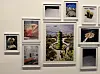 En vit vägg med flera inramade bilder, inklusive ett stort centralt fotografi och mindre verk runtom.