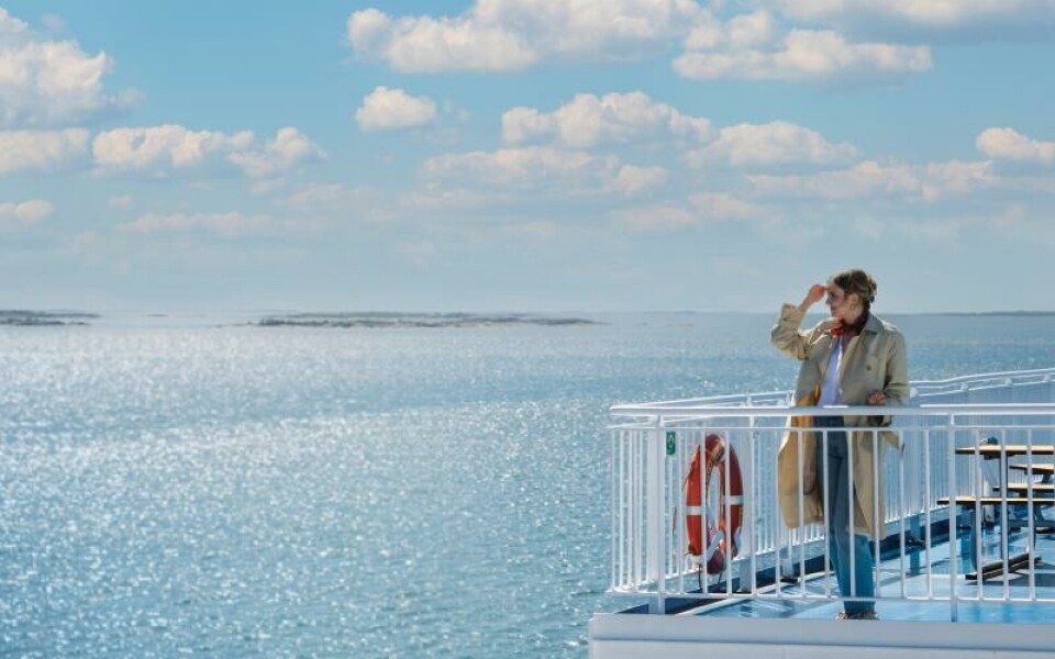 Njut av skärgården tillsammans med Finnlines Kvinna som står på däck i vackert väder och tittar ut över skärgården