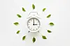 Green leaves around white alarm clock on light table background. Time change concept. Closeup. Top down view.