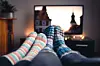 Couple with socks and woolen stockings watching movies or series on tv in winter. Woman and man sitting or lying together on sofa couch in home living room using online streaming service in television