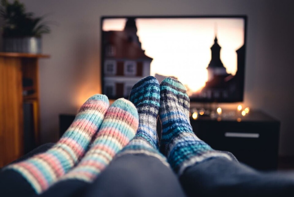 Här är höstens filmer och serier! Couple with socks and woolen stockings watching movies or series on tv in winter. Woman and man sitting or lying together on sofa couch in home living room using online streaming service in television
