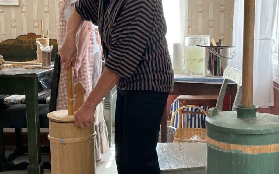 På Jan Karlsgården demonstrerades i somras smörkärning. Här är det Ann-Kristin Karlsson i arbete vid kärnan. I bakgrunden skymtar Sig-Britt Fagerström som berättade om smörkärnandet och förevisade resultatet.Foto:
